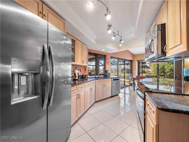 kitchen featuring stainless steel appliances, light brown cabinetry, dark stone countertops, and a raised ceiling