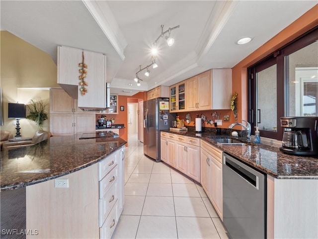 kitchen with stainless steel appliances, dark stone counters, light brown cabinetry, a raised ceiling, and light tile patterned floors