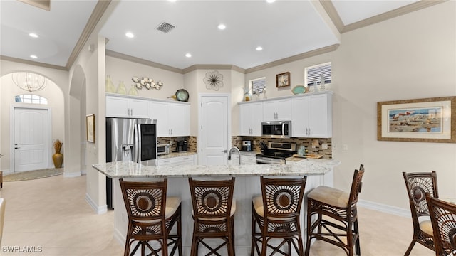 kitchen with white cabinets, light stone counters, a kitchen bar, and stainless steel appliances