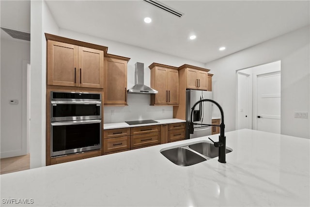 kitchen featuring light stone countertops, stainless steel appliances, wall chimney exhaust hood, and sink