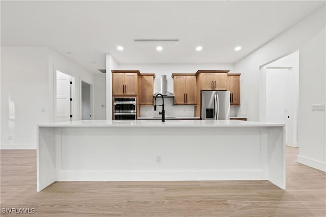 kitchen featuring appliances with stainless steel finishes, light hardwood / wood-style floors, wall chimney exhaust hood, and a large island