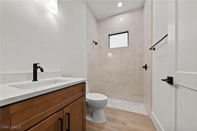 bathroom with hardwood / wood-style flooring, vanity, toilet, and tiled shower