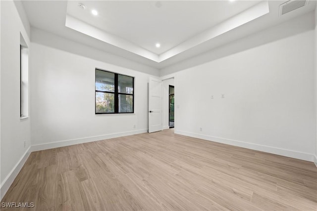 spare room featuring a tray ceiling and light hardwood / wood-style flooring