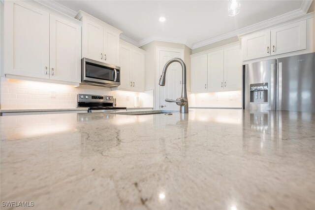 kitchen with backsplash, ornamental molding, appliances with stainless steel finishes, light stone counters, and white cabinetry