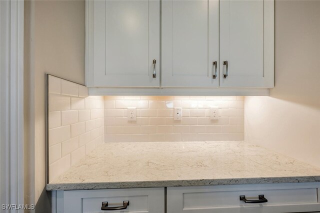 kitchen featuring light stone countertops, decorative backsplash, and white cabinets