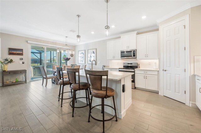 kitchen with a breakfast bar, stainless steel appliances, a center island with sink, white cabinets, and hanging light fixtures