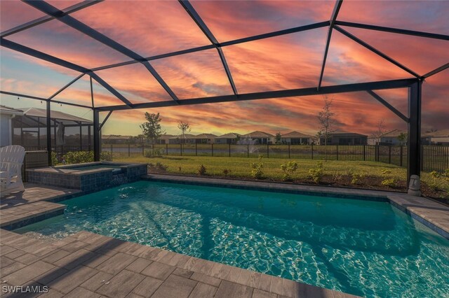 pool at dusk with a lanai, a patio area, an in ground hot tub, and a yard