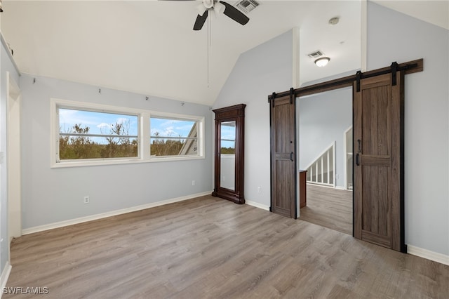 unfurnished bedroom featuring ceiling fan, a barn door, light wood-type flooring, and lofted ceiling