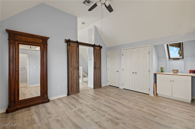 unfurnished bedroom with ceiling fan, a barn door, high vaulted ceiling, light hardwood / wood-style floors, and multiple closets