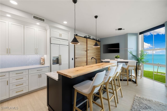 kitchen with a breakfast bar, paneled fridge, white cabinets, a kitchen island, and hanging light fixtures