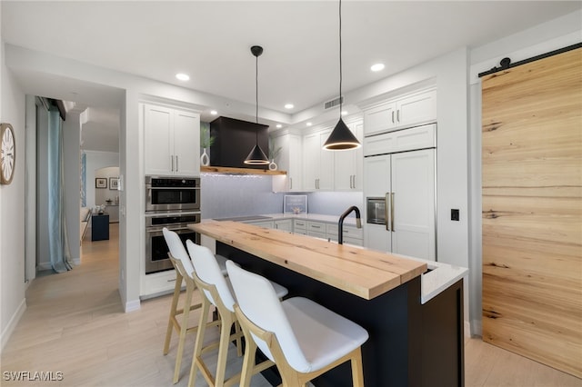 kitchen with wood counters, a barn door, white cabinets, a kitchen island, and hanging light fixtures