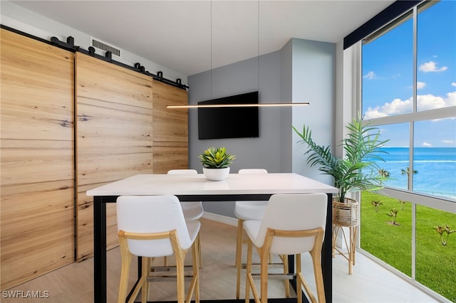 dining area with a barn door, a wealth of natural light, floor to ceiling windows, and light wood-type flooring