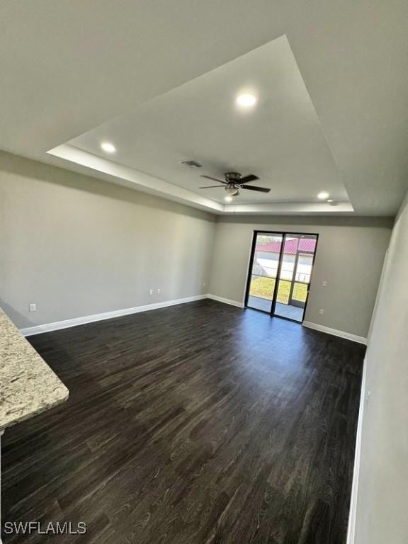 empty room with a tray ceiling, ceiling fan, and dark hardwood / wood-style flooring