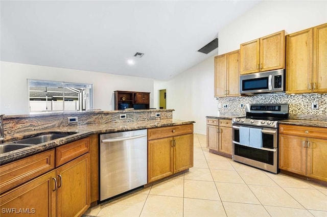 kitchen with backsplash, stainless steel appliances, sink, dark stone countertops, and light tile patterned flooring