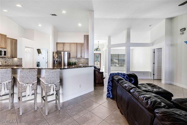 kitchen featuring backsplash, dark stone counters, tile patterned floors, appliances with stainless steel finishes, and kitchen peninsula