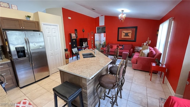 kitchen with sink, stainless steel fridge, a kitchen bar, light tile patterned floors, and a center island with sink