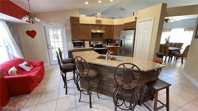 kitchen with sink, appliances with stainless steel finishes, an island with sink, decorative backsplash, and decorative light fixtures