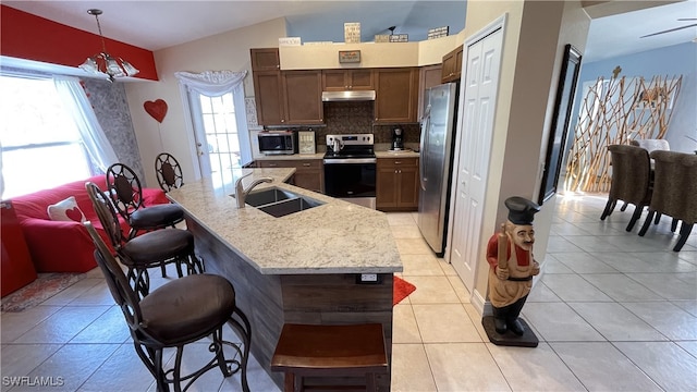 kitchen with vaulted ceiling, pendant lighting, an island with sink, sink, and stainless steel appliances