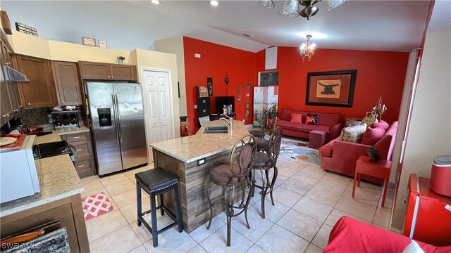 kitchen featuring sink, stainless steel refrigerator with ice dispenser, an island with sink, a kitchen bar, and vaulted ceiling