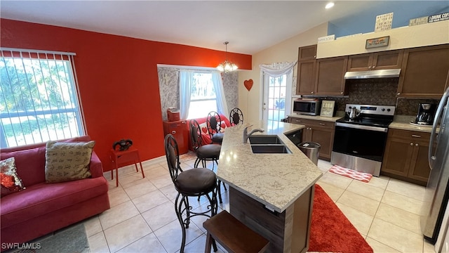 kitchen featuring sink, a kitchen island with sink, stainless steel appliances, decorative light fixtures, and vaulted ceiling