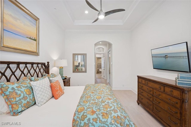 bedroom with a raised ceiling, ceiling fan, light wood-type flooring, ornamental molding, and connected bathroom