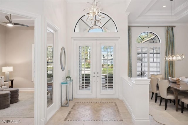 tiled foyer featuring french doors, ceiling fan with notable chandelier, a tray ceiling, and ornamental molding