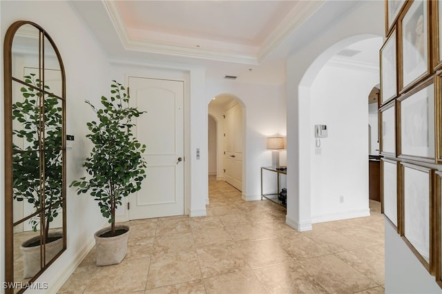 hall with a raised ceiling and ornamental molding