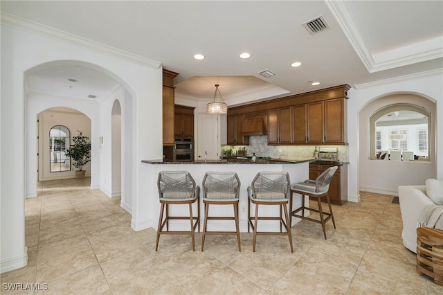 kitchen featuring tasteful backsplash, dark stone countertops, hanging light fixtures, and ornamental molding