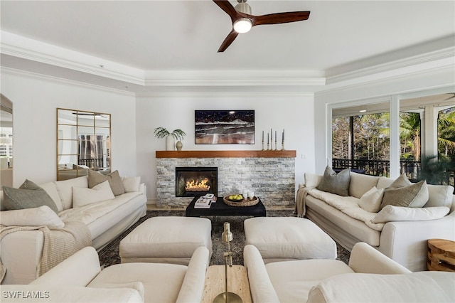 living room with a stone fireplace, ceiling fan, and crown molding