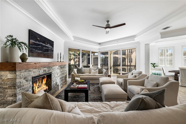 living room with ceiling fan, a stone fireplace, and ornamental molding