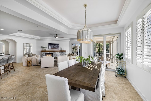 tiled dining area featuring ceiling fan with notable chandelier, a raised ceiling, ornamental molding, and a fireplace