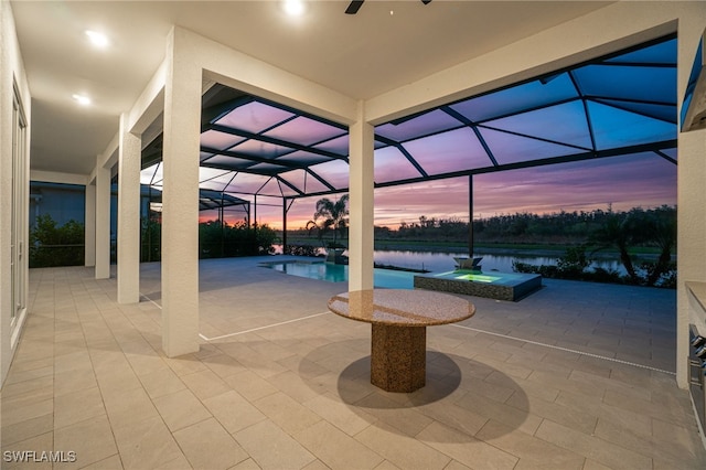 patio terrace at dusk featuring a lanai, a water view, and a pool with hot tub