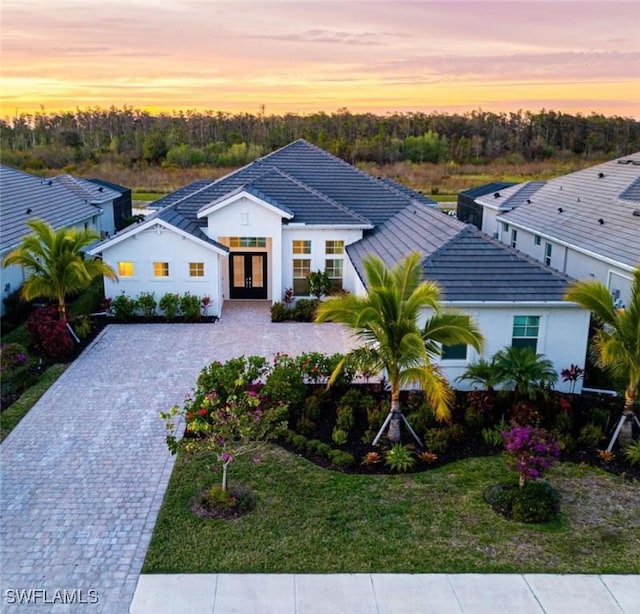 view of front of home with a tiled roof, french doors, decorative driveway, stucco siding, and a front yard