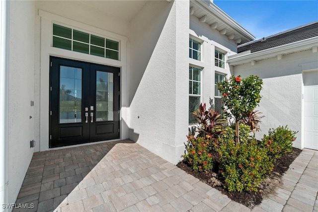 doorway to property featuring french doors, an attached garage, and stucco siding