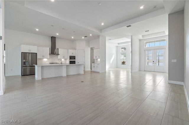 unfurnished living room featuring a towering ceiling, sink, a tray ceiling, and french doors