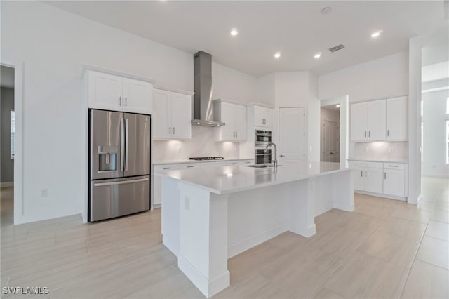 kitchen featuring a center island with sink, white cabinetry, wall chimney range hood, and stainless steel appliances