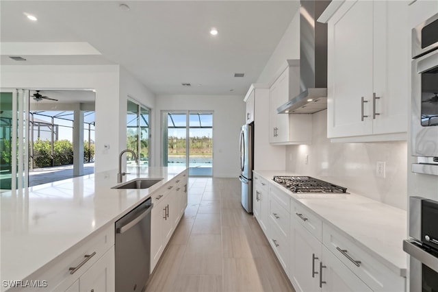 kitchen featuring white cabinets, wall chimney exhaust hood, ceiling fan, light stone counters, and stainless steel appliances