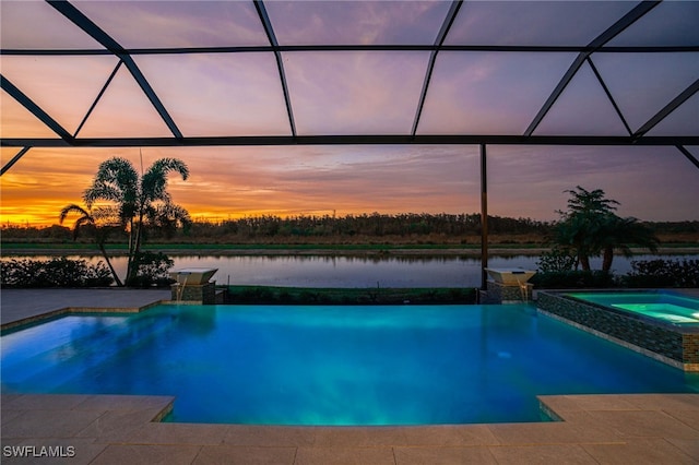 pool at dusk featuring a lanai, an in ground hot tub, and a water view