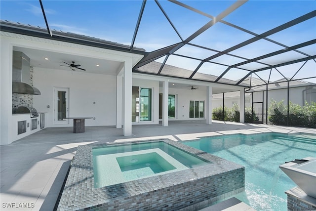 view of pool featuring a pool with connected hot tub, glass enclosure, a patio, and an outdoor kitchen