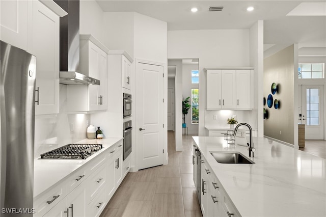 kitchen featuring visible vents, appliances with stainless steel finishes, wall chimney range hood, white cabinetry, and a sink