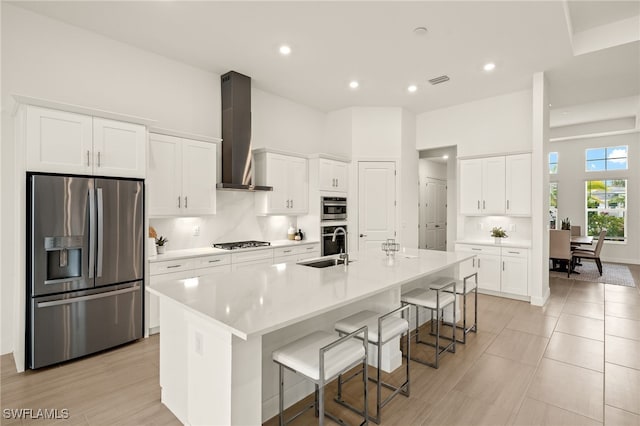 kitchen featuring a breakfast bar, white cabinetry, appliances with stainless steel finishes, wall chimney range hood, and a large island with sink