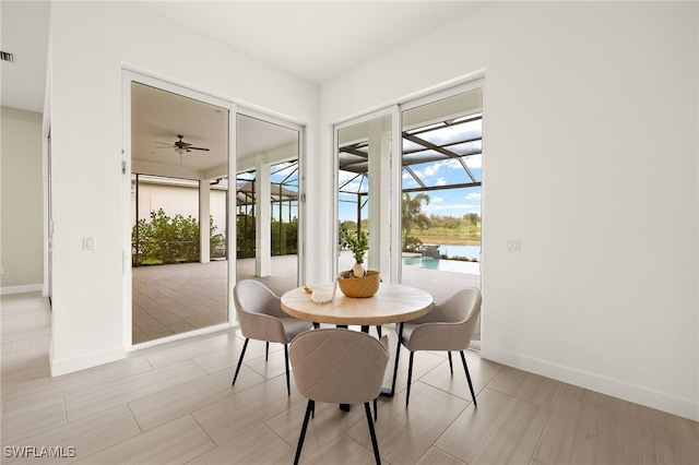 dining space featuring a sunroom, a water view, visible vents, and baseboards