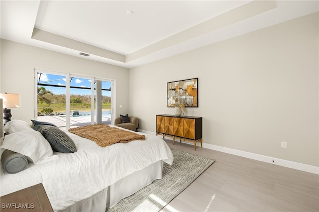 bedroom with baseboards, a raised ceiling, visible vents, and access to exterior