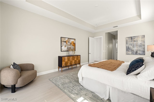 bedroom with light wood finished floors, visible vents, baseboards, and a raised ceiling