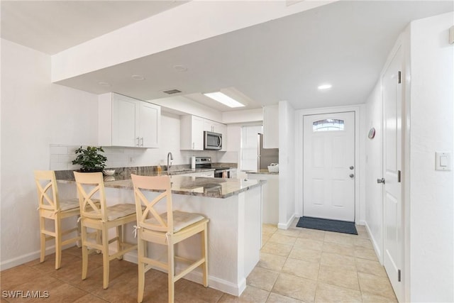 kitchen featuring white cabinets, dark stone countertops, a kitchen bar, kitchen peninsula, and stainless steel appliances