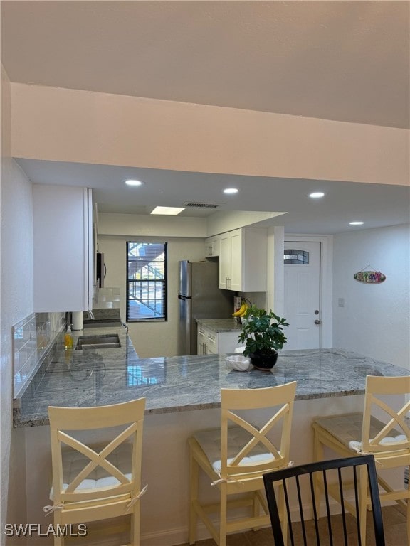 kitchen with stainless steel appliances, tasteful backsplash, kitchen peninsula, a kitchen bar, and white cabinets