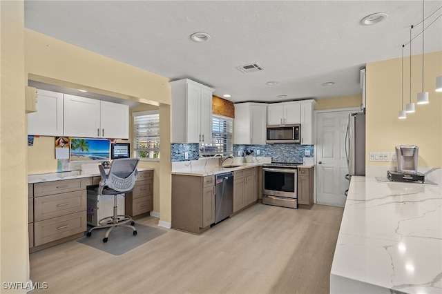 kitchen featuring light stone countertops, appliances with stainless steel finishes, light wood-type flooring, pendant lighting, and white cabinetry