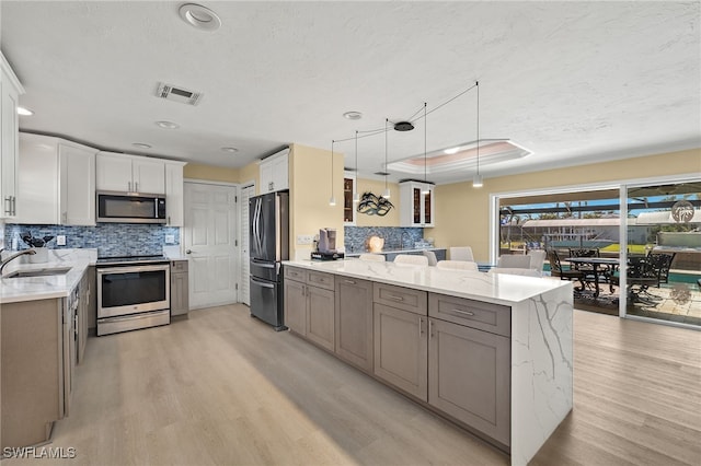 kitchen featuring light stone countertops, white cabinetry, pendant lighting, and stainless steel appliances