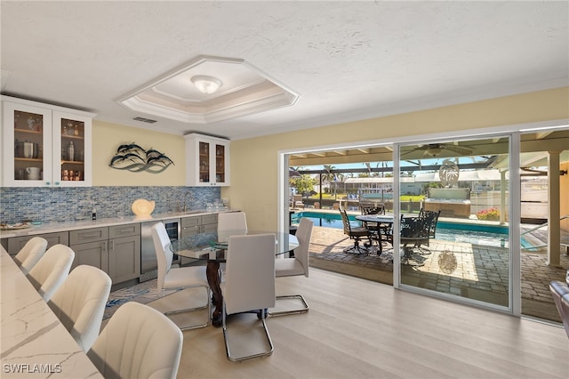 dining space featuring indoor wet bar, a raised ceiling, light wood-type flooring, and a textured ceiling