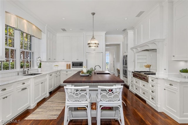 kitchen with light stone counters, sink, built in appliances, decorative light fixtures, and dark hardwood / wood-style floors